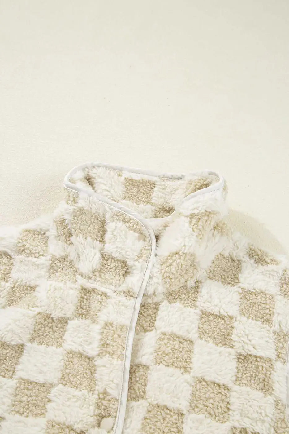 Close-up of a checkered Sherpa Fleece Vest with a neutral color scheme on a beige background