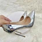 Close-up of hand holding Silver Snake‑Effect Stiletto Heels, showing detailed snake texture and glossy silver finish for party wear.