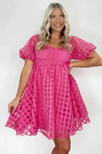 Front-facing model in strawberry pink checkered babydoll dress with A-line silhouette and sheer puff sleeves, perfect for summer styling.