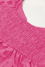 Detailed view of smocked back panel on strawberry pink babydoll dress, showcasing stretch fit and textured design.