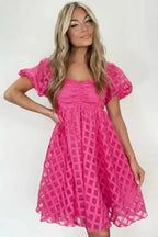 Model wearing strawberry pink checkered babydoll dress with ruched bust and flared skirt, ideal for Valentine's Day or casual wear.