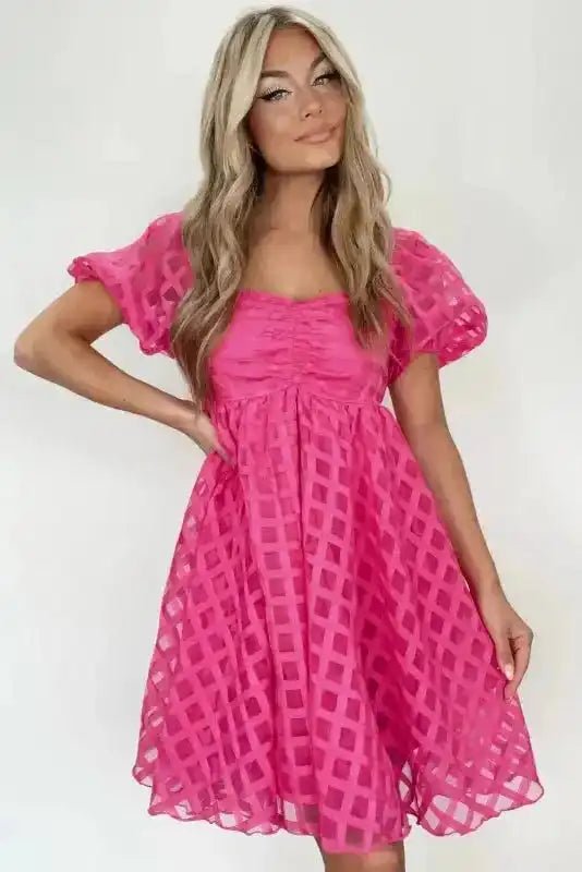 Model wearing strawberry pink checkered babydoll dress with ruched bust and flared skirt, ideal for Valentine's Day or casual wear.