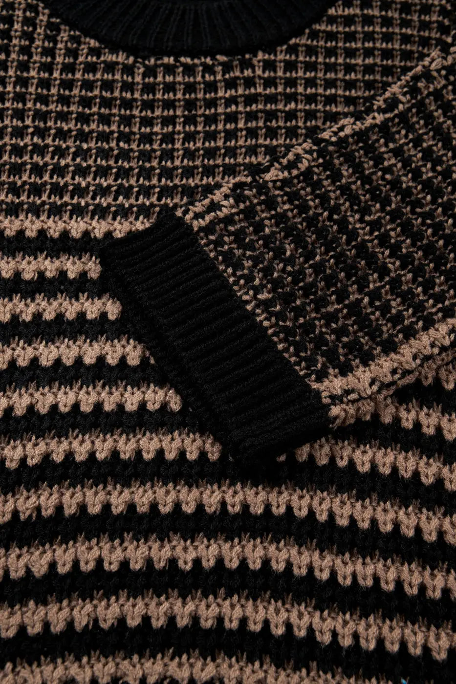 Detail of sleeve and striped knit pattern on black and taupe slouchy jumper. Soft, breathable fabric with ribbed cuff for summer styling.