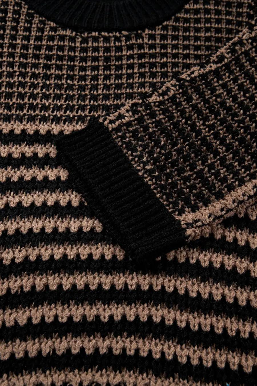 Detail of sleeve and striped knit pattern on black and taupe slouchy jumper. Soft, breathable fabric with ribbed cuff for summer styling.