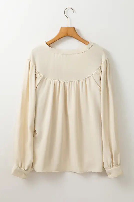 Stylish notched v-neck blouse with gathered yoke on a wooden hanger