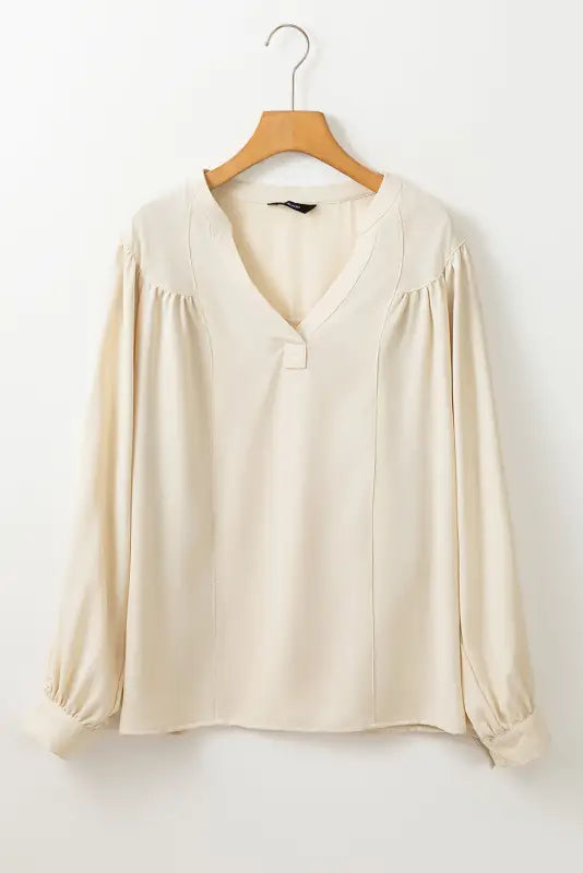 Stylish notched v-neck blouse: cream long-sleeved with gathered shoulders on wooden hanger