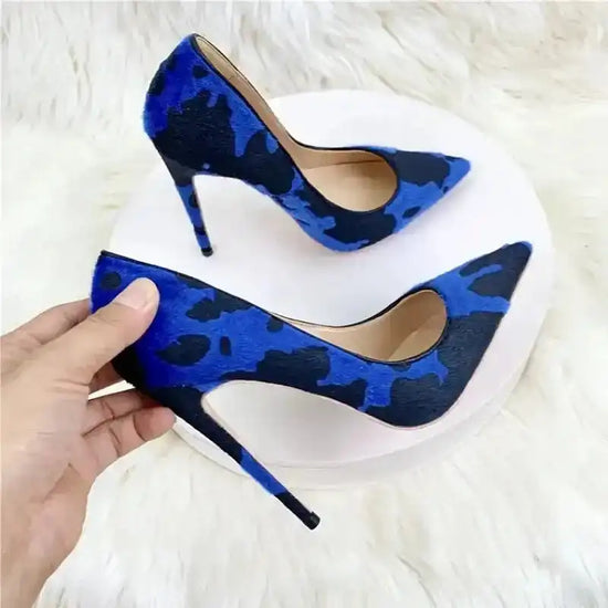 Hand holding Blue‑Black Graffiti Suede Heels with high stiletto heel and graffiti pattern. Elegant pumps for stylish women.