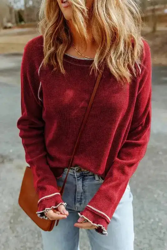 Front view of red Round Neck Textured Top with raw edge seams and long sleeves, styled casually with light denim jeans.