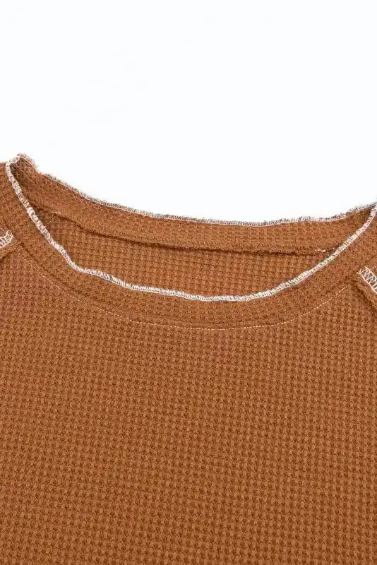 Close-up of brown round neckline with exposed stitching, highlighting the textured knit and casual finish.