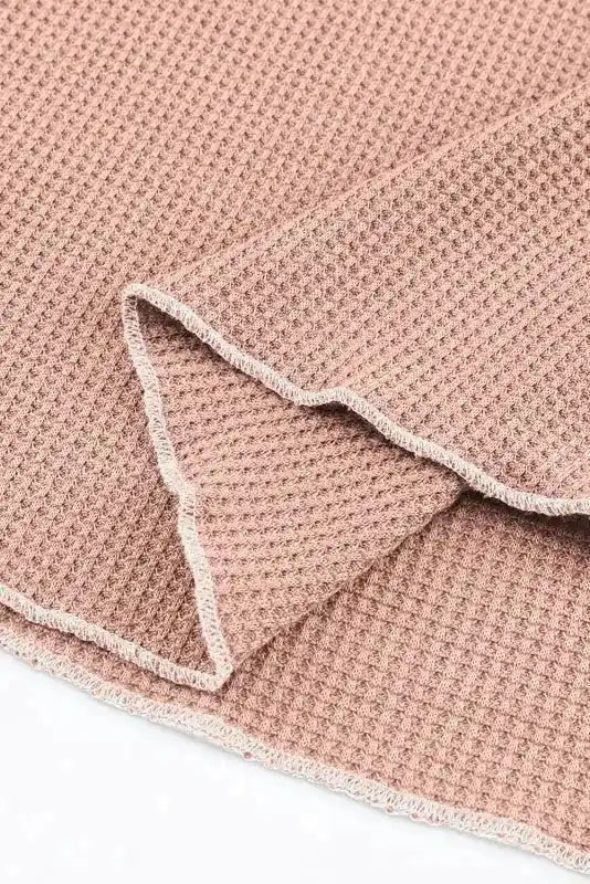 Detailed view of apricot pink textured hem with raw edge finish, emphasizing the top's casual and bohemian style.