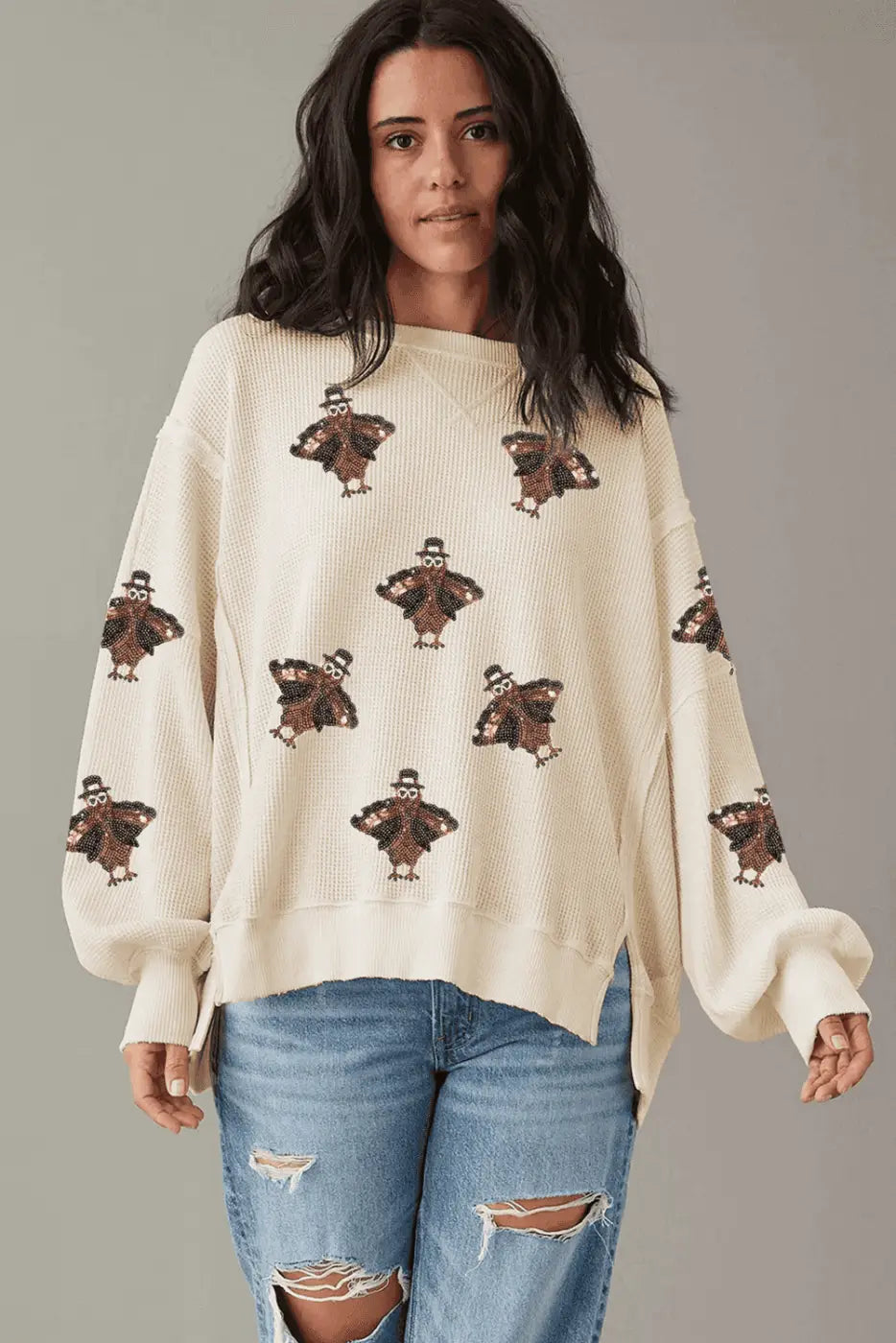 Woman wearing a cream sweater with teddy bear patterns and blue jeans on a gray background