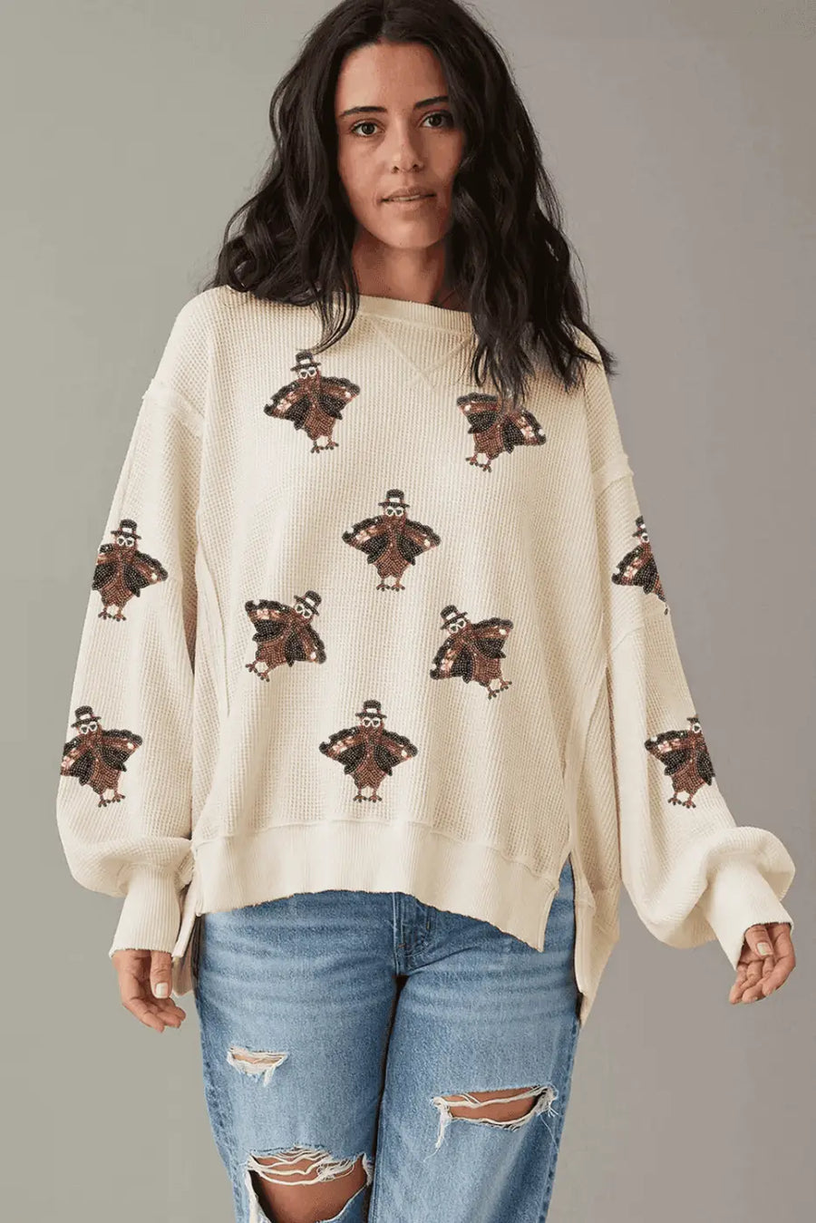 Woman wearing a cream sweater with teddy bear patterns and blue jeans on a gray background