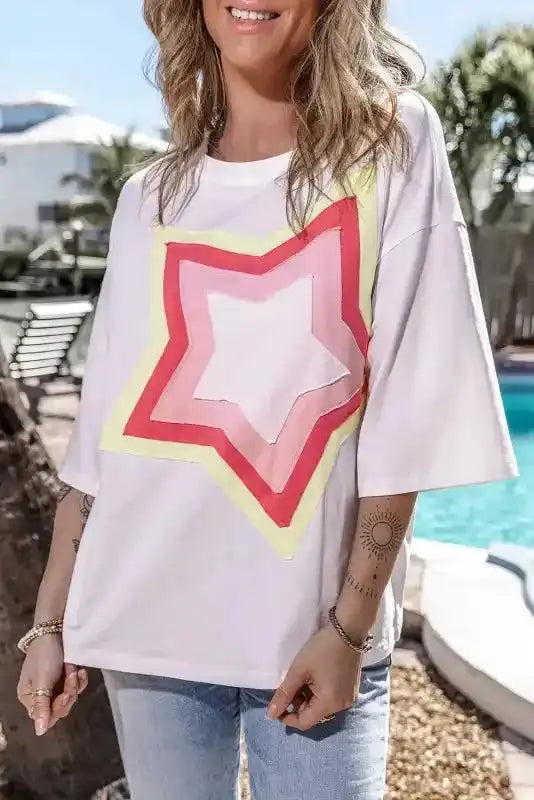 White oversized T-shirt with vibrant star patch design in red, pink, and yellow. Half sleeves and relaxed silhouette for comfy casual look.