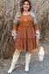 Smiling woman in rust-colored waffle ruffle plus mini dress, gray hat, and white boots