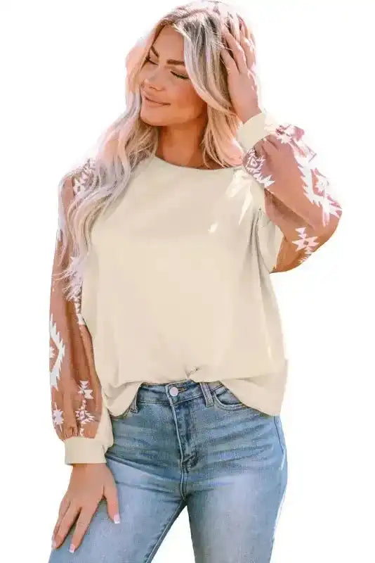 Studio shot of Western Print Patch Long Sleeve Top with beige body and brown Aztec sleeves, styled with jeans for a casual look.
