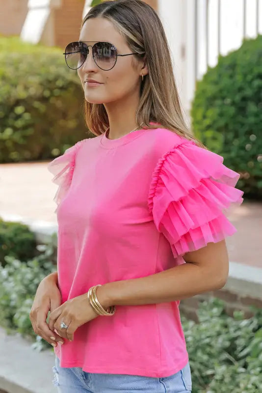 Woman in whimsical wave blouse, bright pink top with tulle ruffle sleeves, sunglasses on