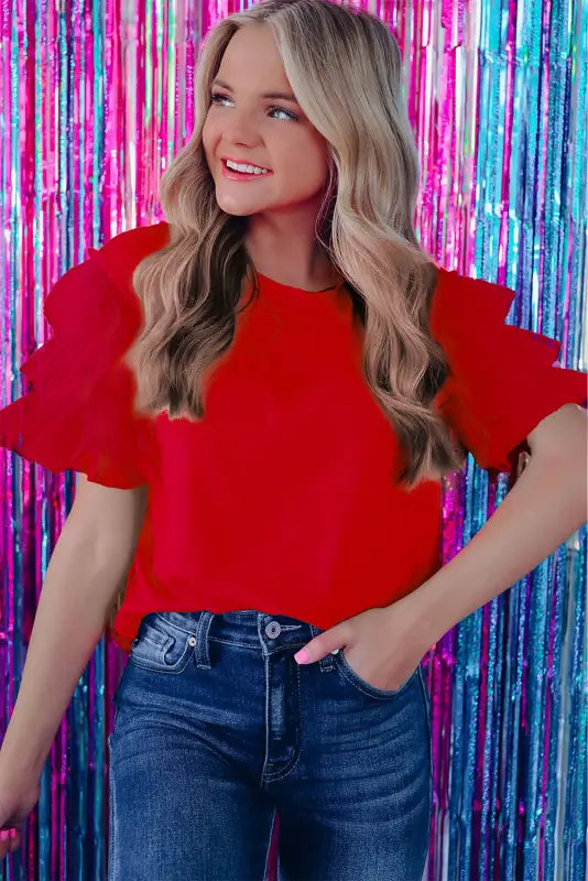 Woman in whimsical wave blouse, long blonde hair, colorful backdrop, red top, blue jeans