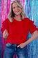 Smiling blonde woman in whimsical wave blouse against a colorful shimmering backdrop