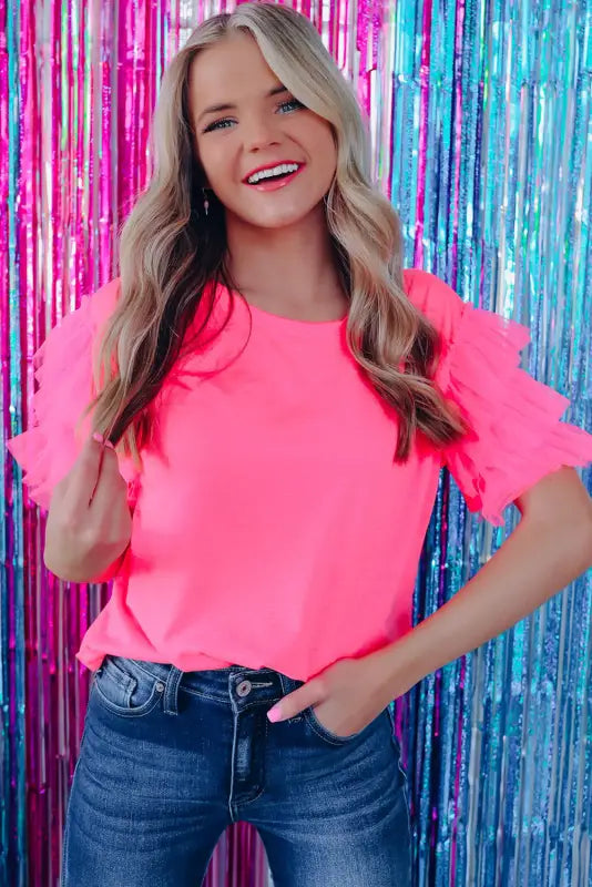 Smiling blonde woman in a bright pink whimsical wave blouse against colorful tinsel backdrop