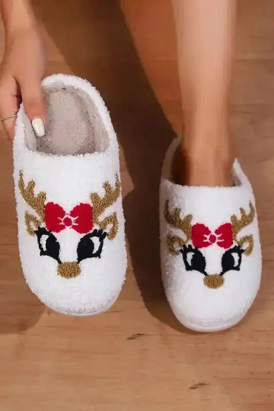 White Christmas deer slippers with red bow and antlers, soft fleece design for festive indoor comfort and warmth.