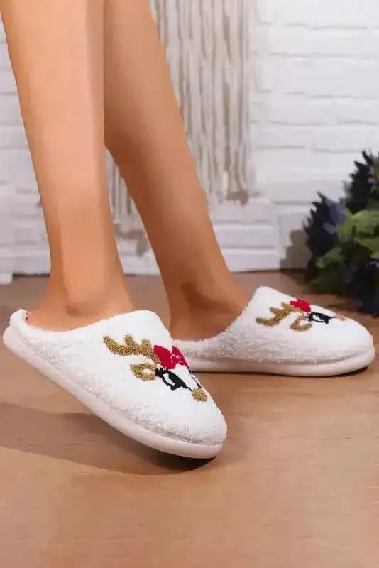 Side view of white plush slippers with cute reindeer face and red bow, ideal for cozy winter wear at home.