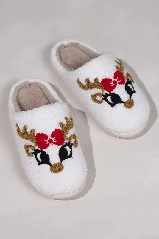 Pair of white Christmas deer slippers with red bows and soft lining, festive fleece footwear for indoor winter use.
