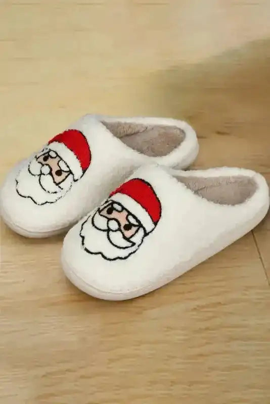 Pair of White Christmas Santa Claus Slippers on wooden floor, showcasing soft fleece fabric and cozy holiday-themed design.