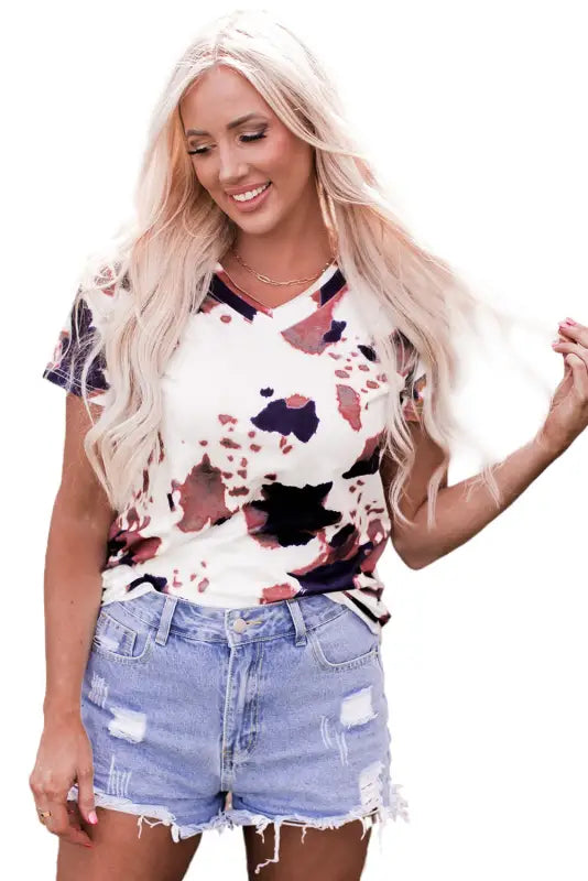 Smiling woman in white cow pattern print short sleeve v neck t shirt and distressed denim shorts