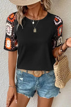 Model wearing black top with floral crochet short sleeves and round neckline