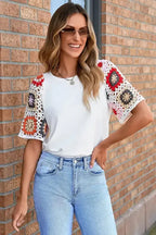 Woman styling white crochet-sleeve top with blue jeans in garden setting