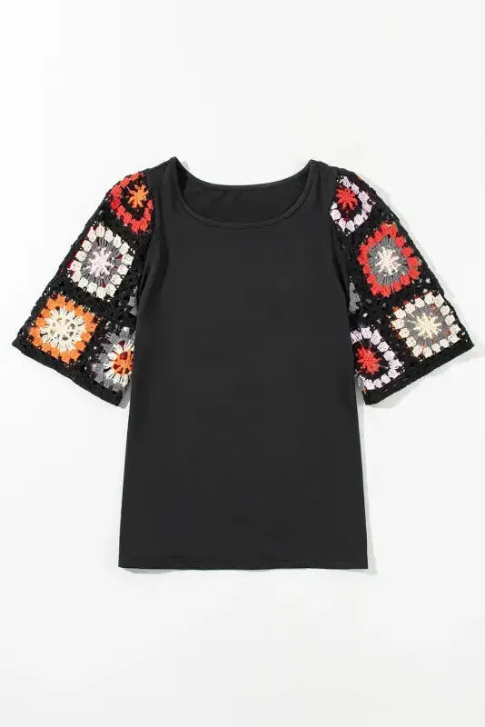 Black short sleeve top with floral crochet detail laid flat on neutral background