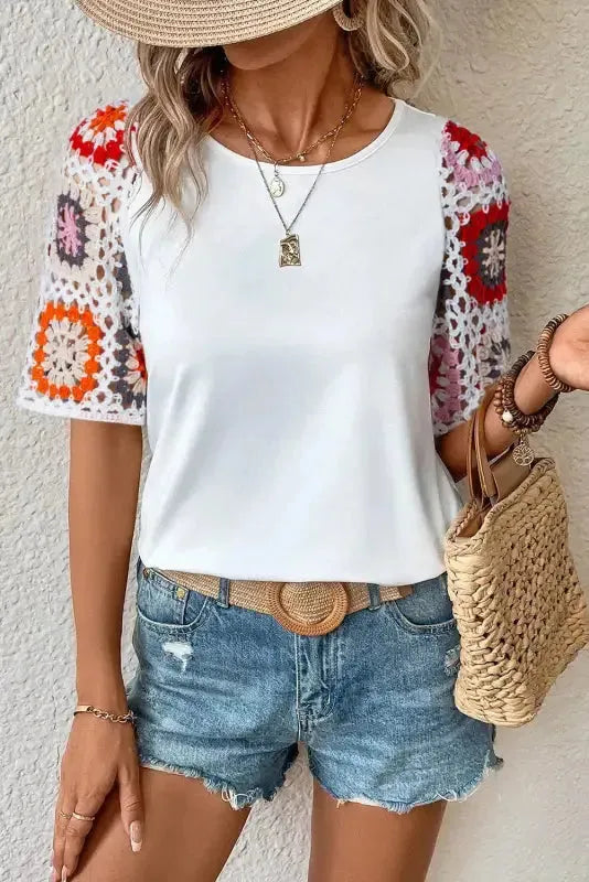 Model wearing white top with floral crochet short sleeves and round neckline