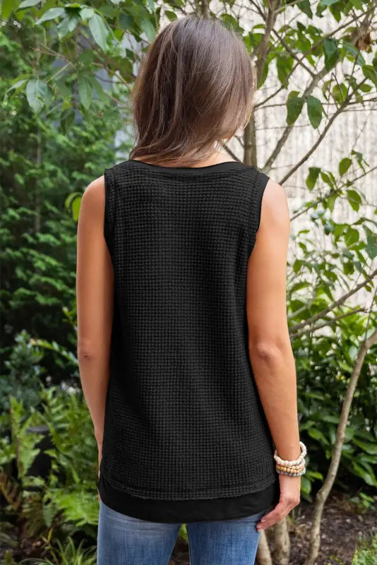 Person with long brown hair in black waffle-knit top, wearing white flowy tunic tank top