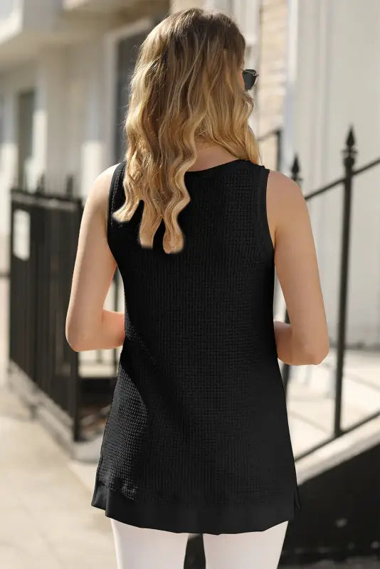 Woman with long blonde wavy hair wearing black sleeveless knit top and white flowy tunic tank top