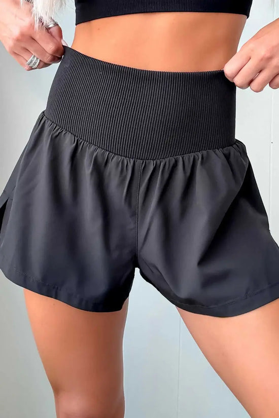 White ribbed high waist athletic shorts for women featuring a wide ribbed waistband and flowy patchwork design. Ideal for workouts and summer wear.