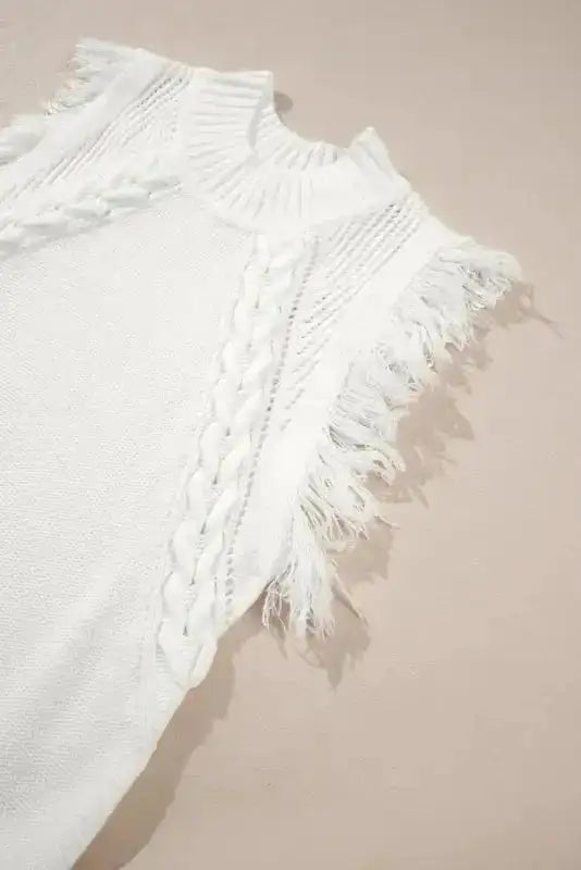 Close-up of white woven knit tank top showing braided knit pattern and tassel fringe on armholes, highlighting boho summer details.