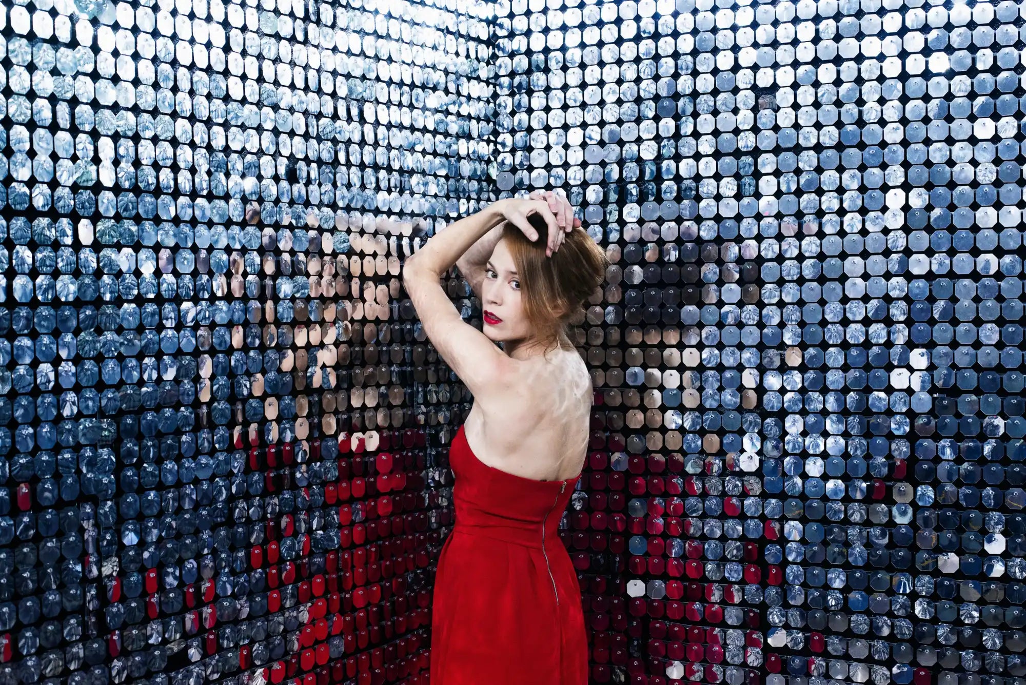 A figure in a vibrant red dress poses against a shimmering backdrop.